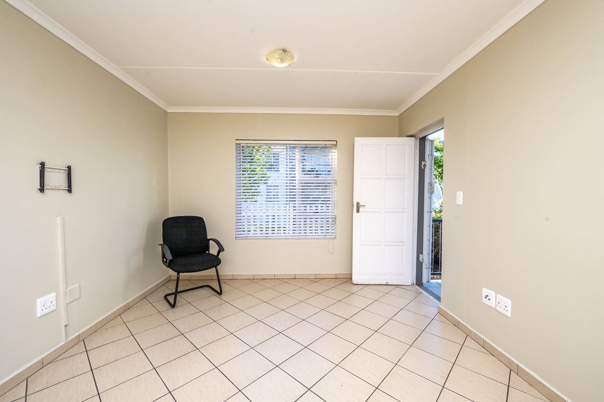 A bright, empty living area featuring neutral tiled flooring, a wall-mounted TV bracket, and direct access to an outdoor space.
