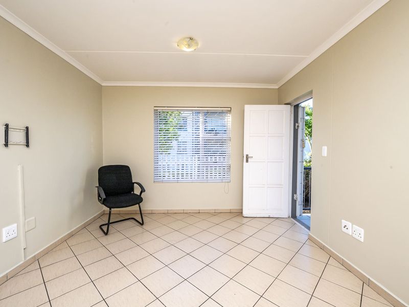 A bright, empty living area featuring neutral tiled flooring, a wall-mounted TV bracket, and direct access to an outdoor space.