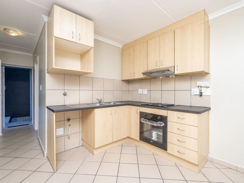 A clean, functional kitchen featuring light wood-finish cabinetry, dark countertops, built-in oven, gas hob, and tiled flooring.