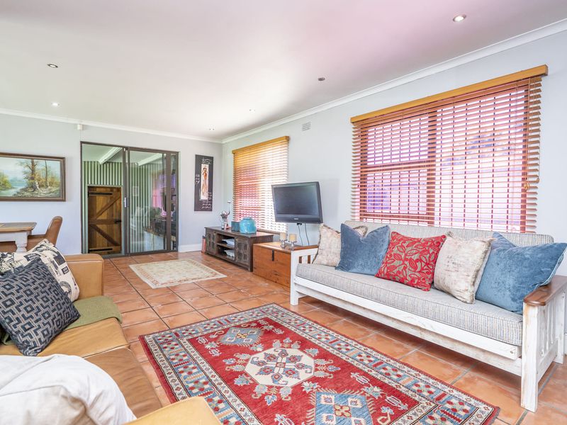 A spacious living room featuring terracotta floor tiles, recessed downlighting, and large windows with venetian blinds, providing a bright and comfortable living space.