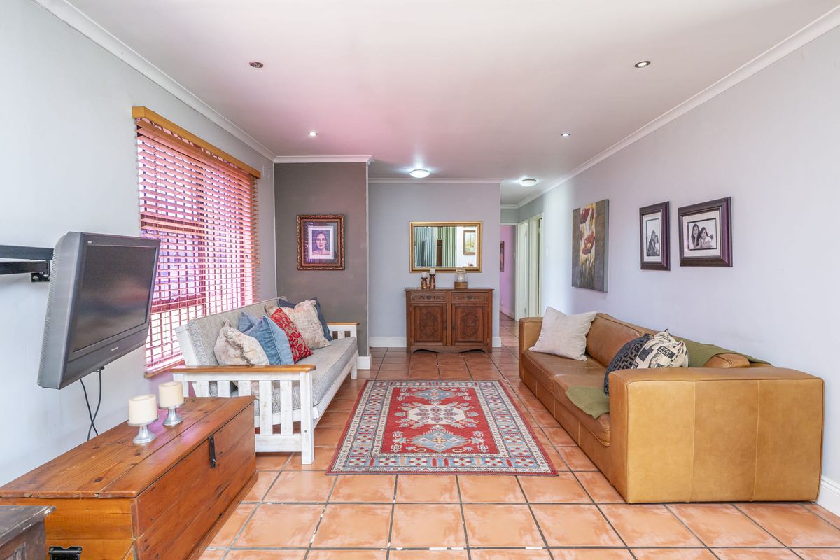 A spacious living room featuring terracotta floor tiles, recessed downlighting, and large windows with venetian blinds, offering a comfortable and functional living space.