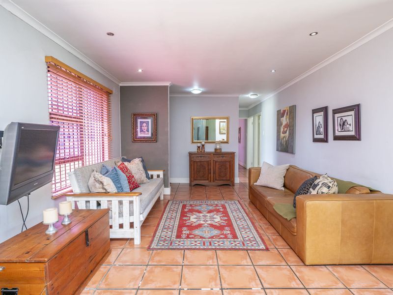 A spacious living room featuring terracotta floor tiles, recessed downlighting, and large windows with venetian blinds, offering a comfortable and functional living space.