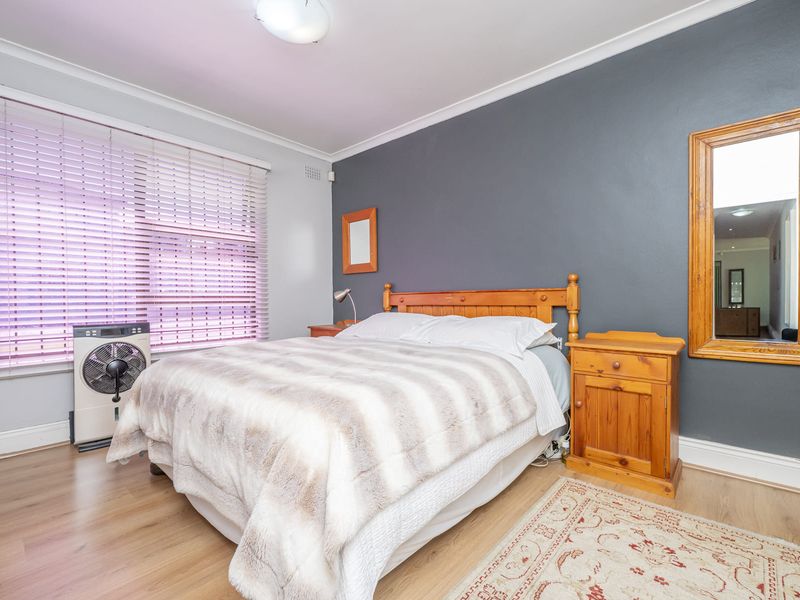 A well-lit bedroom featuring laminate flooring, a dark accent wall, and venetian blinds, providing a functional and comfortable sleeping space.
