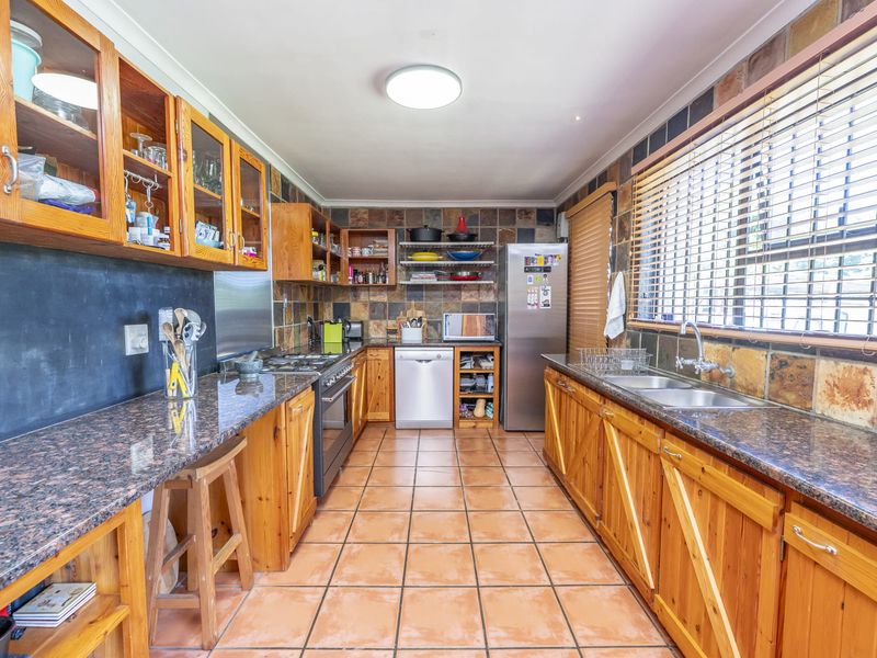 A functional kitchen featuring wooden cabinetry, granite countertops, stone wall cladding, and tiled flooring, offering a classic, rustic aesthetic with ample storage space.