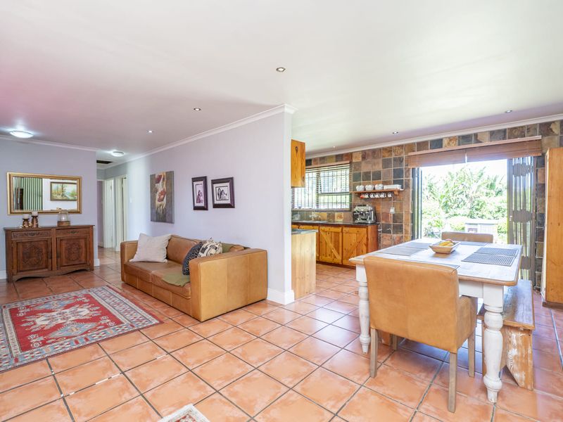 Open-plan living and dining area featuring terracotta floor tiles, recessed lighting, and a functional kitchen with stone tile backsplash and wooden cabinetry.