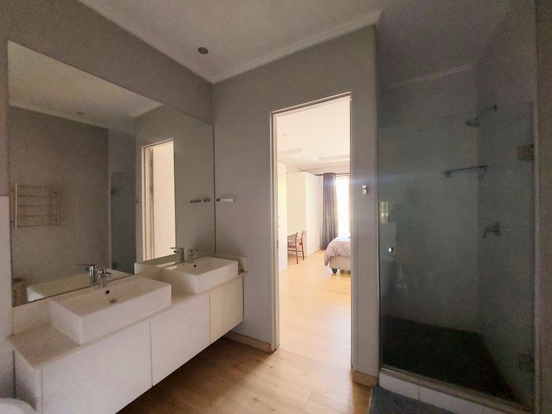 Modern bathroom featuring a double vanity with integrated sinks, large wall mirror, and a glass-enclosed shower, with direct access to the bedroom.
