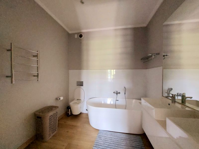 Modern bathroom featuring a freestanding bathtub, wall-mounted toilet, and a double vanity with a large mirror and heated towel rail.