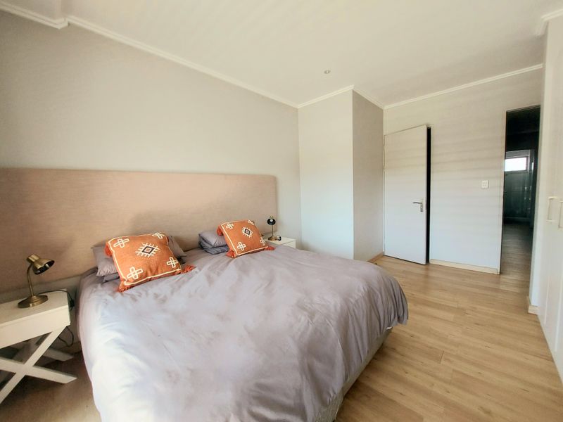 A well-maintained bedroom featuring light laminate flooring, a neutral color palette, and a built-in headboard, providing a clean and comfortable living space.
