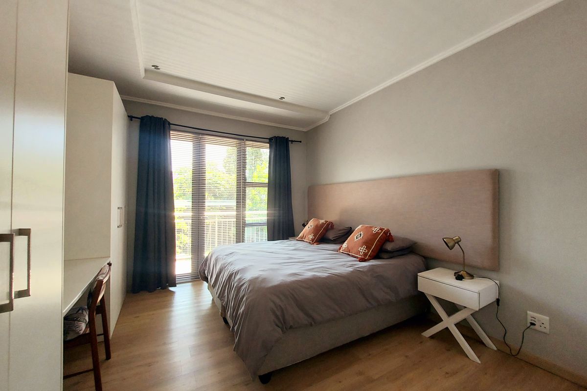 A well-maintained bedroom featuring laminate flooring, recessed ceiling lighting, a built-in wardrobe, and a sliding glass door providing access to a balcony.