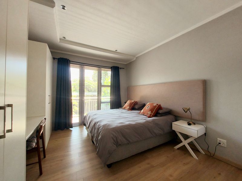 A well-maintained bedroom featuring laminate flooring, recessed ceiling lighting, a built-in wardrobe, and a sliding glass door providing access to a balcony.
