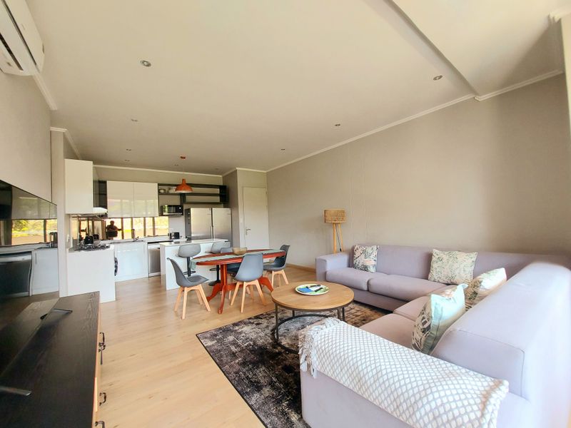 Spacious open-plan living area featuring a modern kitchen with island, laminate flooring, and recessed lighting, creating a bright and functional living space.