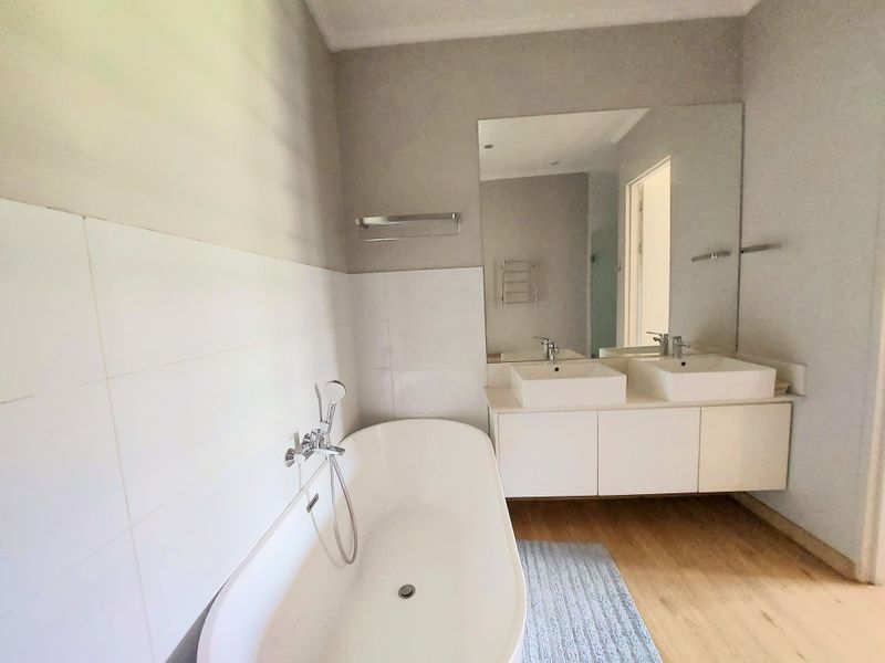 Modern bathroom featuring a sleek freestanding bathtub, double vanity with integrated sinks, and large wall-mounted mirror with neutral wall tiling.