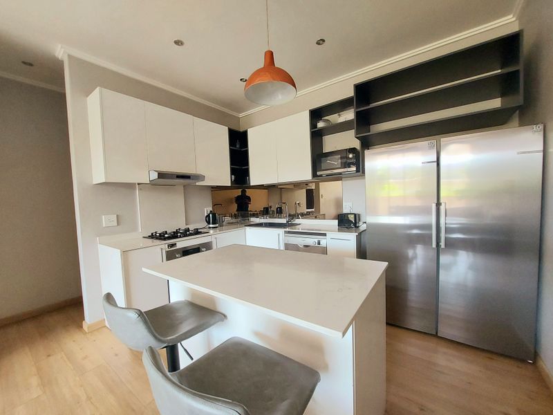 Modern kitchen featuring white cabinetry, quartz countertops, a central island, gas hob, and integrated appliances, offering a clean and functional cooking space.