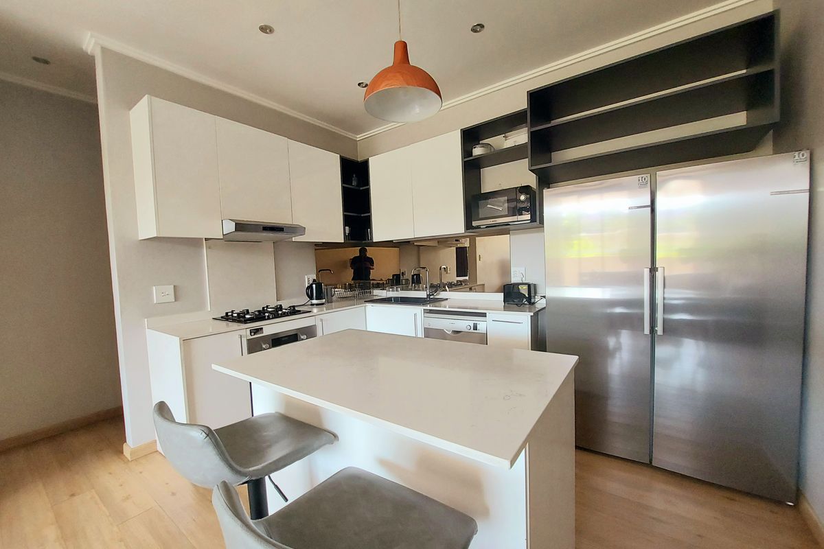 Modern kitchen featuring white cabinetry, quartz countertops, a central island, gas hob, and integrated appliances, offering a clean and functional cooking space.