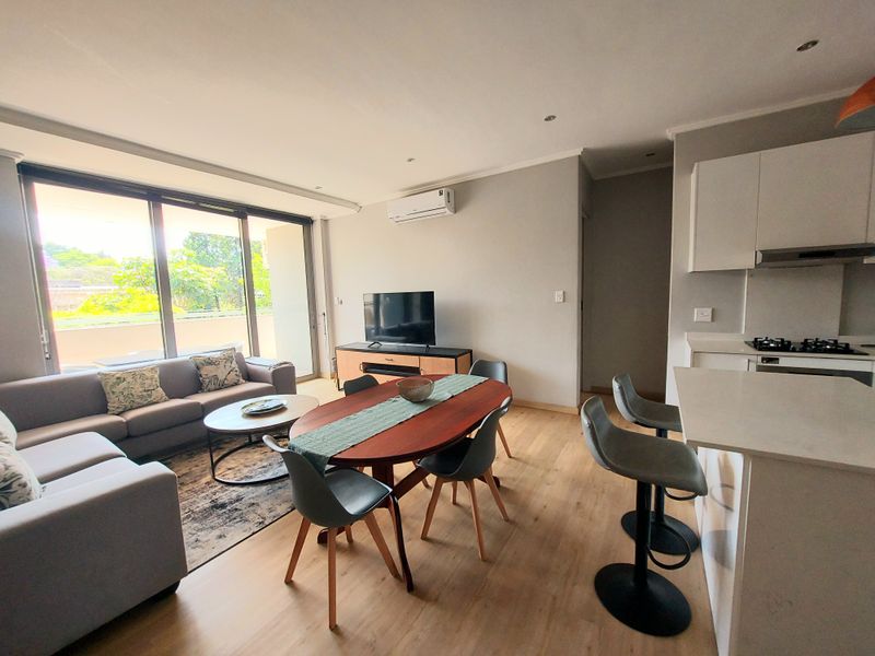 Modern open-plan living area featuring a sleek kitchen with stone countertops, gas hob, and seamless flow to a private balcony through large sliding doors.