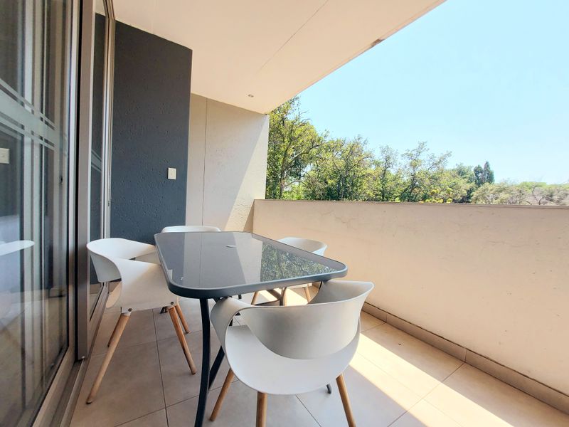 A covered balcony featuring tiled flooring, recessed lighting, and a solid balustrade, offering a pleasant outdoor space with a view of surrounding trees.