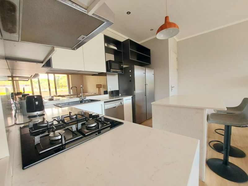 Modern kitchen featuring stone countertops, a gas hob, integrated cabinetry, and a breakfast island, offering a clean and functional cooking space.