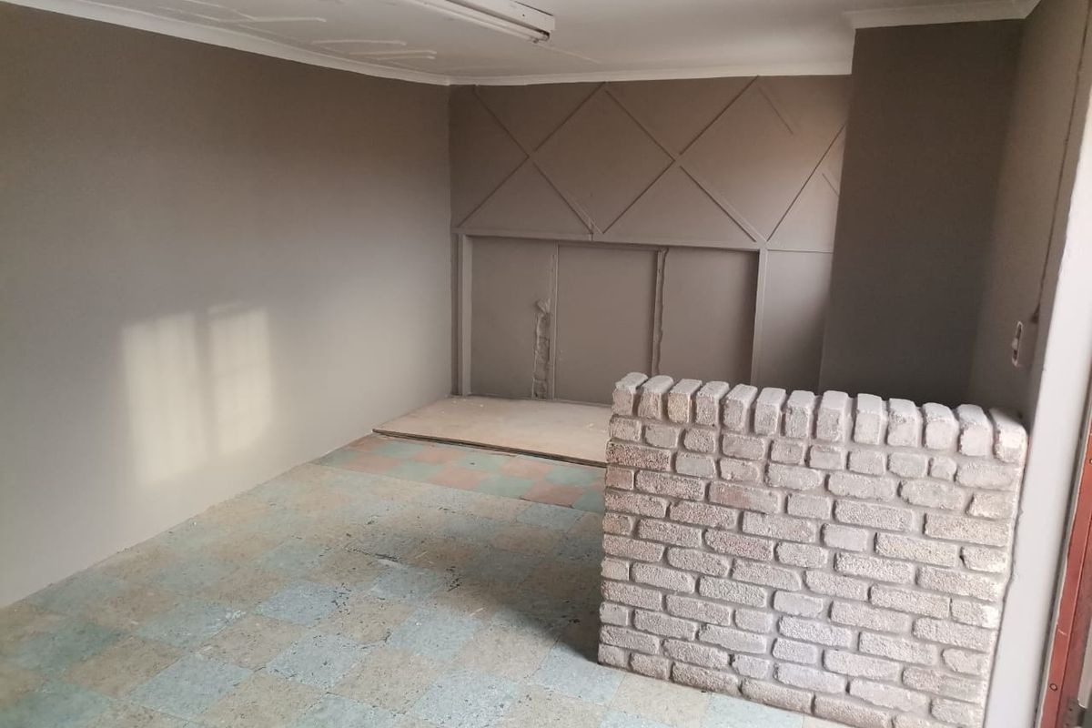 An empty living area featuring a unique brick partition wall, decorative wall paneling, and original tiled flooring, offering a blank canvas for renovation.