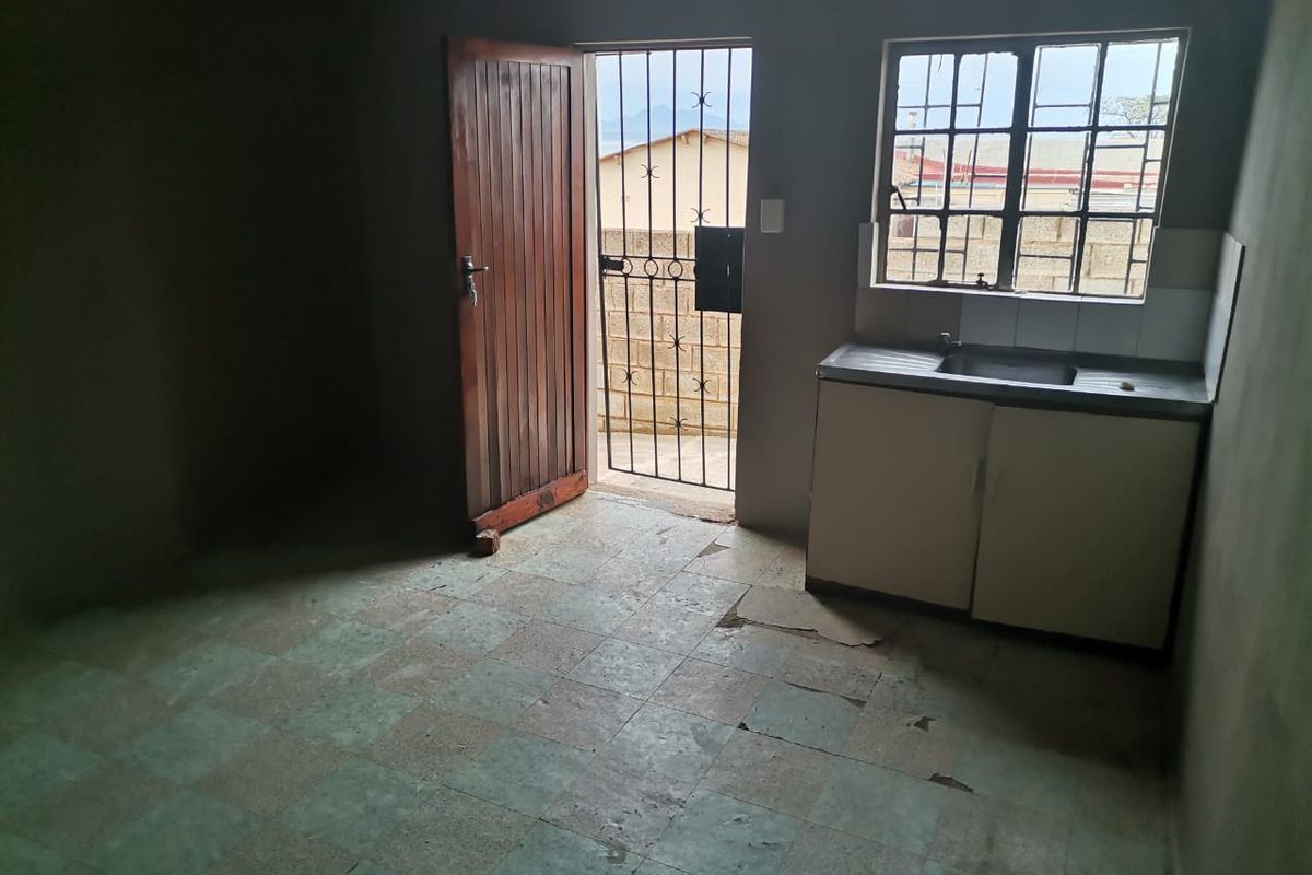 A basic, empty kitchen area featuring a single basin sink, base cabinetry, and direct access to an exterior space via a security gate.