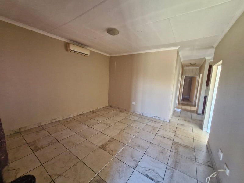 An empty living room featuring tiled flooring and a wall-mounted air conditioning unit, leading into a hallway.