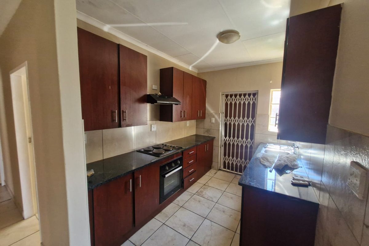 Functional kitchen featuring dark wood cabinetry, granite countertops, built-in oven and hob, and tiled flooring with direct access to an exterior security gate.