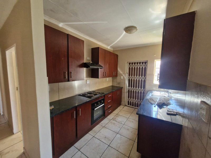 Functional kitchen featuring dark wood cabinetry, granite countertops, built-in oven and hob, and tiled flooring with direct access to an exterior security gate.