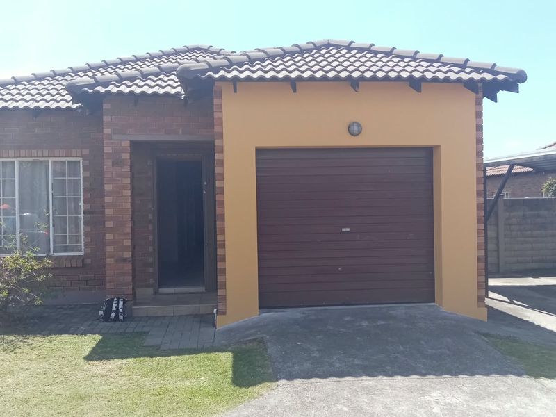 Front elevation of a townhouse featuring a brick and rendered facade, tiled roof, integrated garage, and an adjacent carport structure.