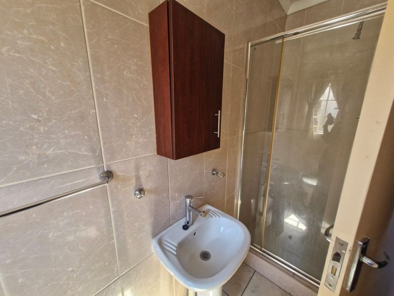 A compact bathroom featuring a pedestal basin, wall-mounted storage cabinet, and a glass-enclosed shower with neutral ceramic wall tiling.
