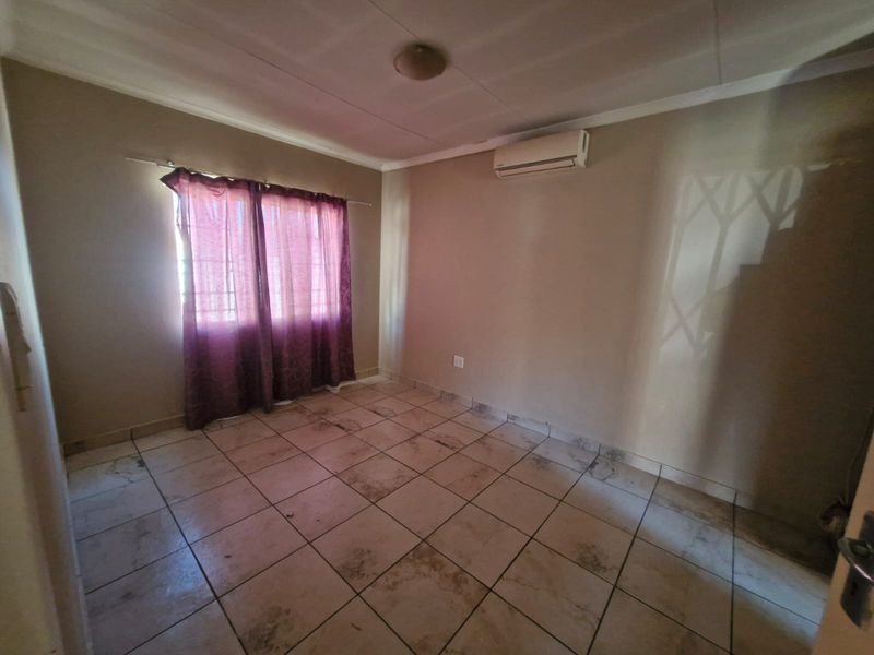 An empty bedroom featuring tiled flooring, a wall-mounted air conditioning unit, and a security gate on the window.