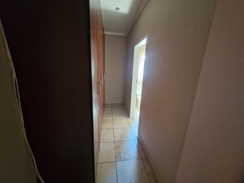 A narrow hallway featuring built-in wooden cupboards and tiled flooring, leading towards an adjacent room.