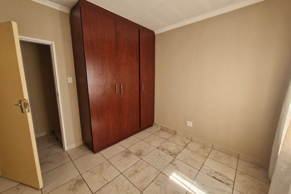 A clean, empty bedroom featuring tiled flooring and a large built-in wooden wardrobe.