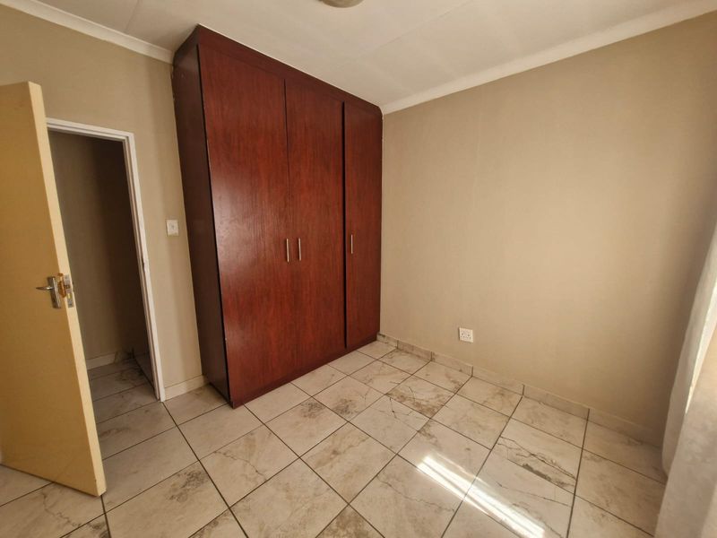 A clean, empty bedroom featuring tiled flooring and a large built-in wooden wardrobe.