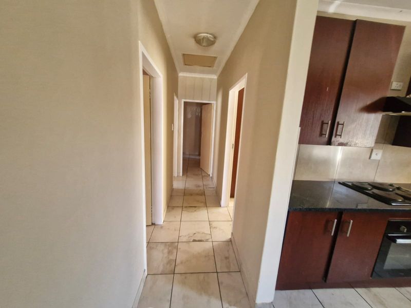 A hallway connecting to adjacent rooms, featuring tiled flooring and an adjacent kitchen area with built-in cabinetry and appliances.