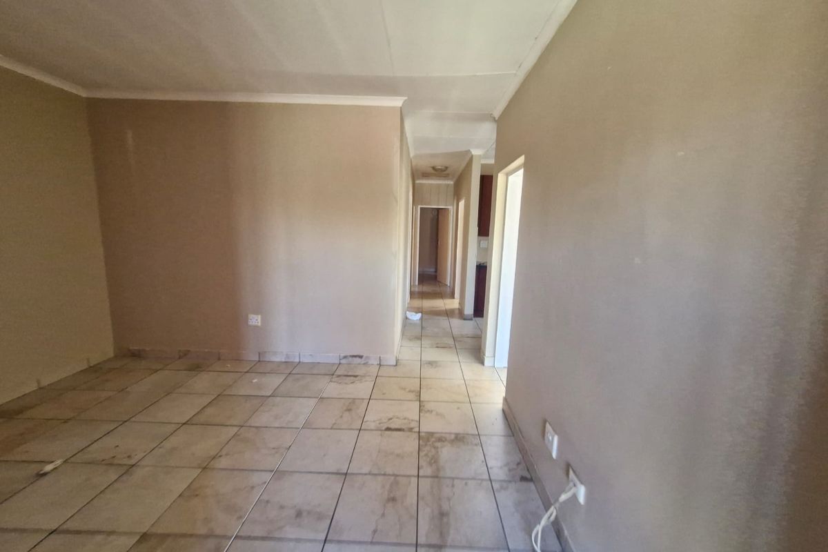 An empty living area featuring ceramic floor tiles and neutral wall paint, leading into a hallway with access to other rooms.