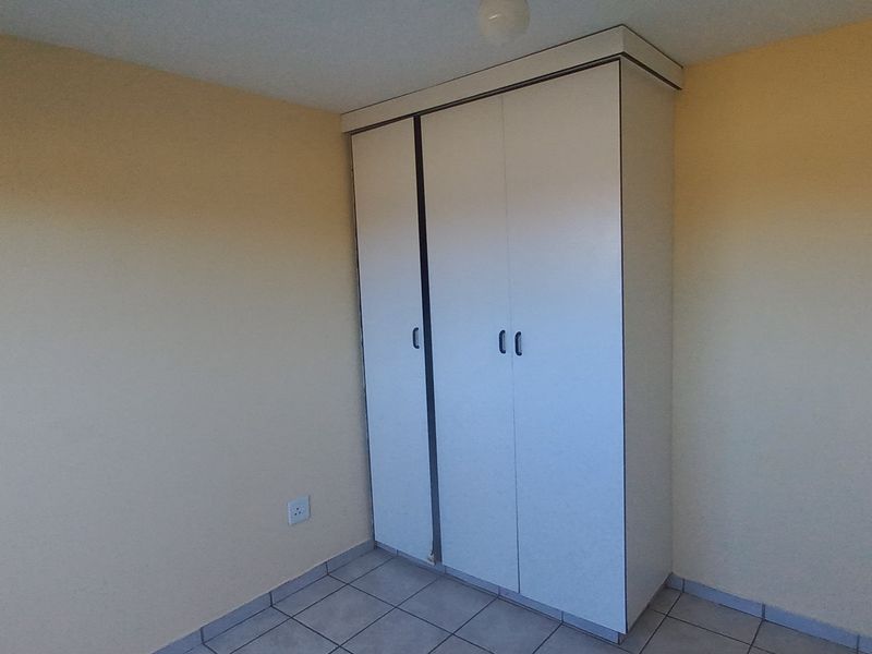 A simple, empty bedroom featuring tiled flooring and a built-in white wardrobe.