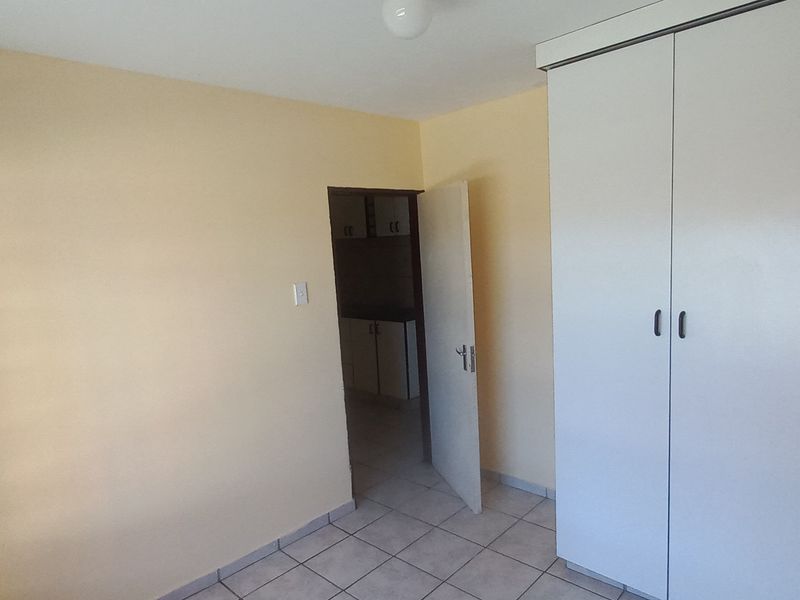 A vacant bedroom featuring neutral wall paint, tiled flooring, and a built-in wardrobe, with a doorway leading to an adjacent kitchen area.