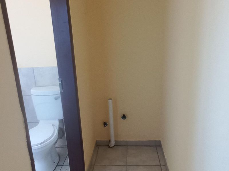 A functional laundry area featuring tiled flooring and dedicated plumbing connections, with an adjacent bathroom visible through the doorway.