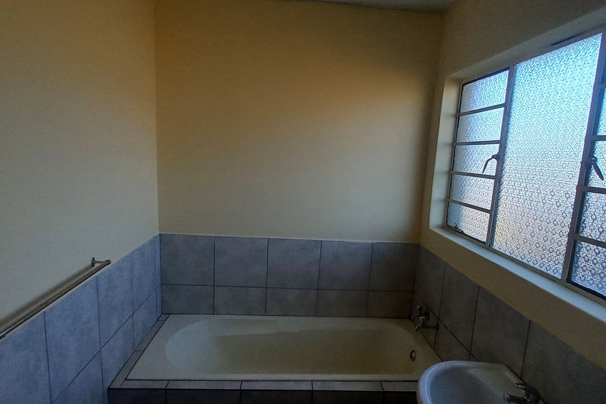 A functional bathroom featuring a built-in bathtub with tiled surround, a pedestal basin, and an obscured glass window for privacy.