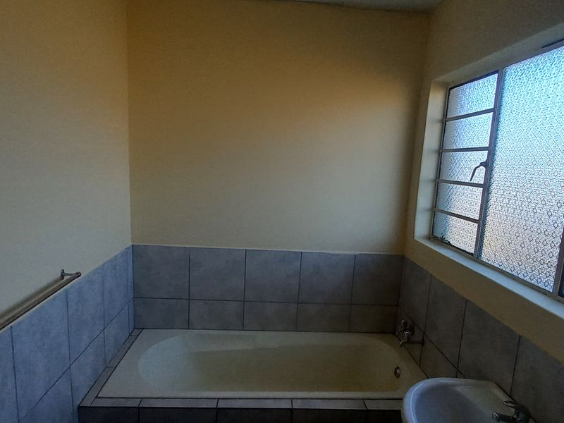 A functional bathroom featuring a built-in bathtub with tiled surround, a pedestal basin, and an obscured glass window for privacy.