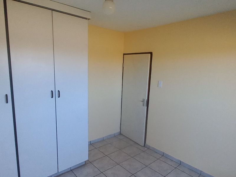 A simple, empty bedroom featuring neutral wall paint, tiled flooring, and a built-in wardrobe.