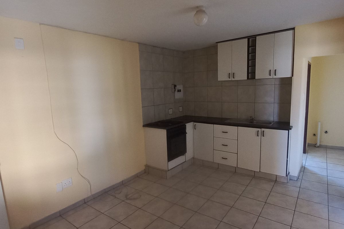 A compact kitchen featuring tiled flooring, built-in cabinetry, a sink, and an integrated oven, requiring minor cosmetic repairs to the wall.