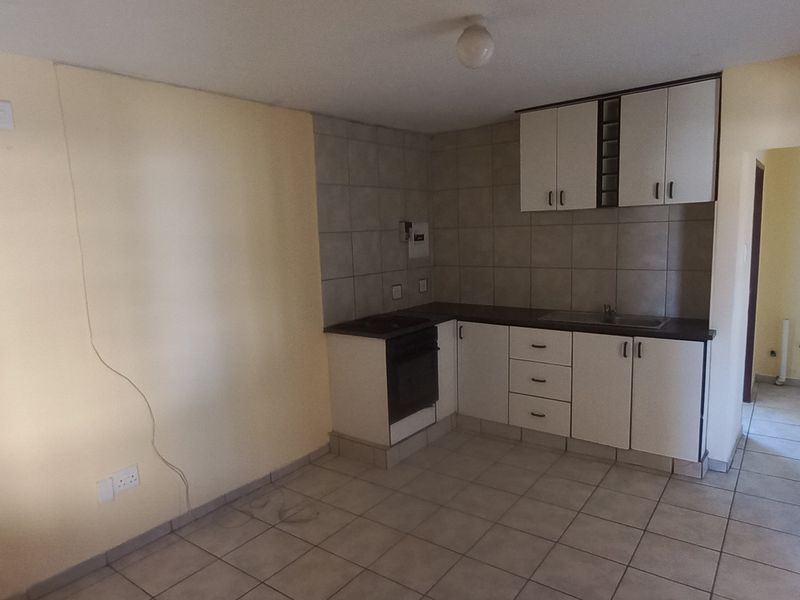A compact kitchen featuring tiled flooring, built-in cabinetry, a sink, and an integrated oven, requiring minor cosmetic repairs to the wall.