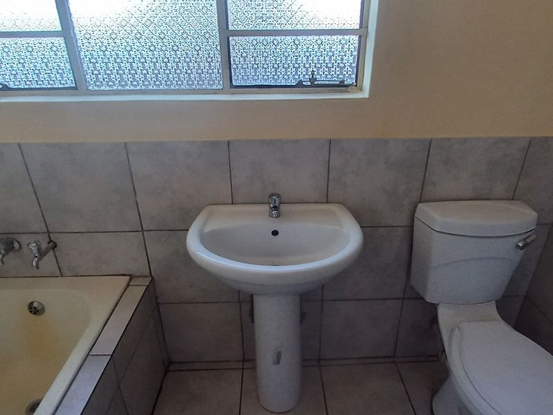 A functional bathroom featuring a pedestal basin, toilet, and built-in bathtub with tiled finishes and an obscured glass window.