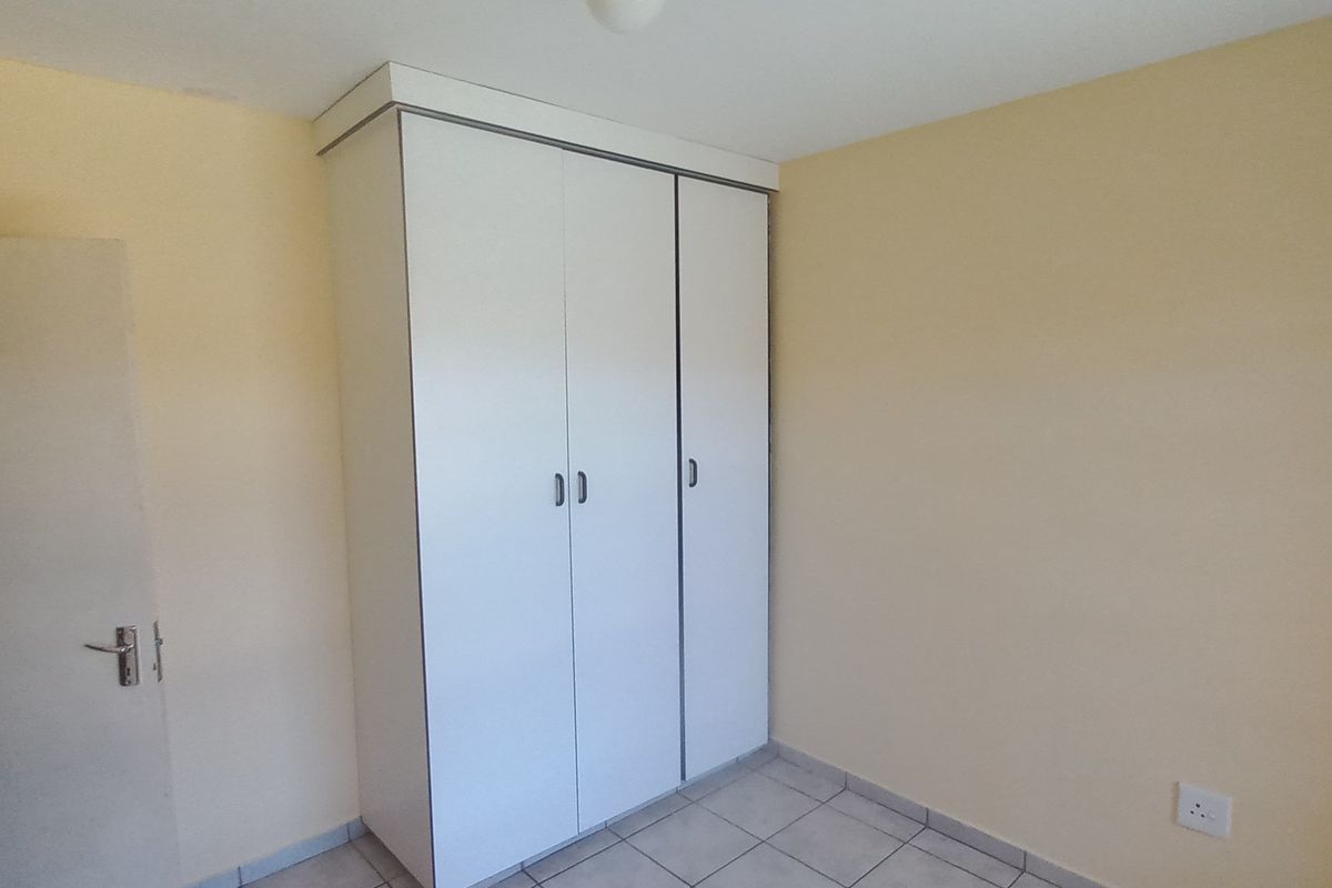 A clean, empty bedroom featuring neutral walls, tiled flooring, and a functional built-in white wardrobe.