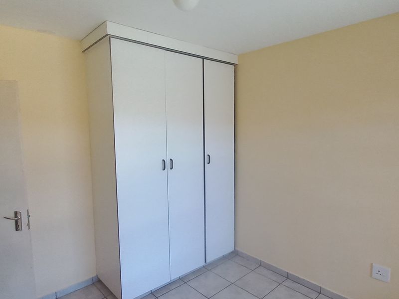 A clean, empty bedroom featuring neutral walls, tiled flooring, and a functional built-in white wardrobe.