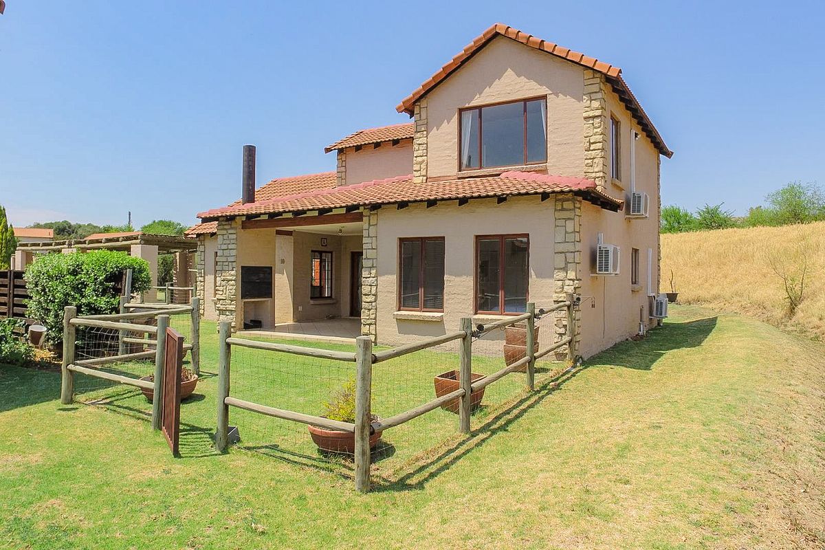 Rear view of a double-storey townhouse featuring stone cladding, a covered patio with a built-in braai, and a private fenced garden area.