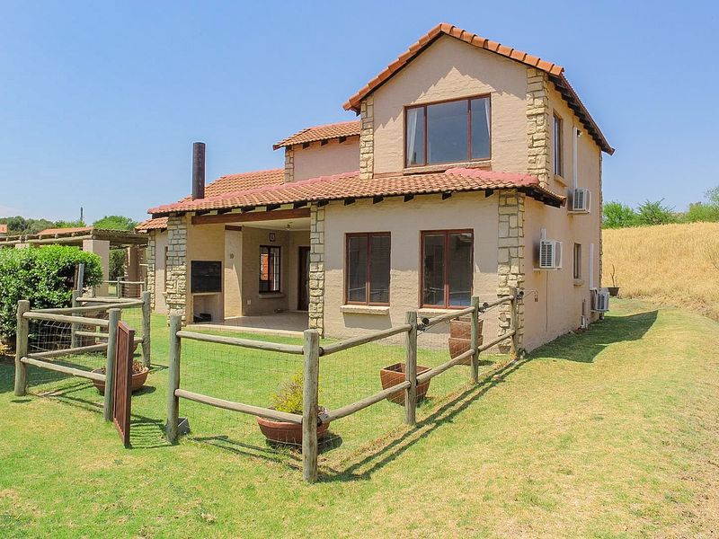 Rear view of a double-storey townhouse featuring stone cladding, a covered patio with a built-in braai, and a private fenced garden area.