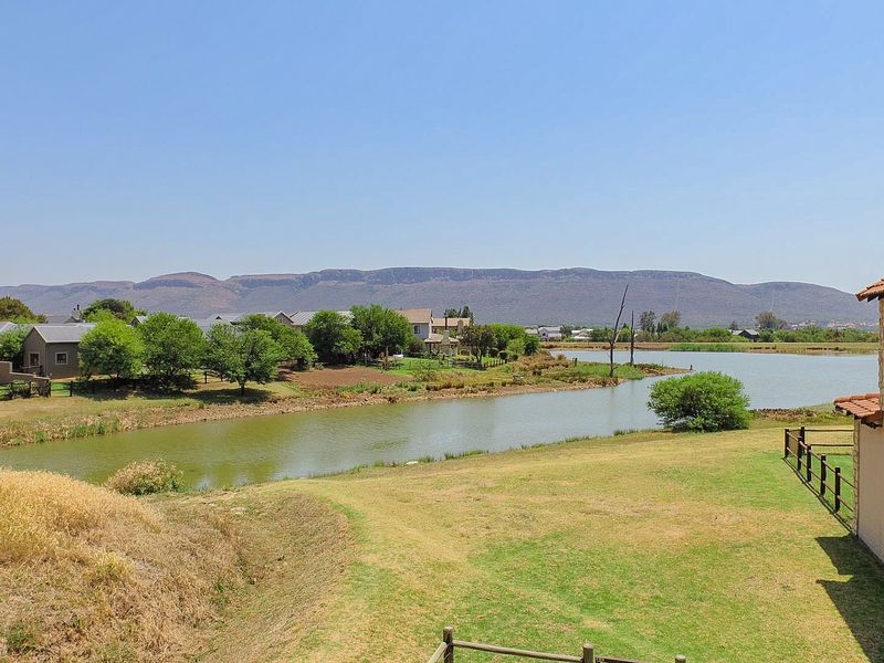Scenic elevated view overlooking a tranquil lake, surrounding estate grounds, and distant mountain range, showcasing the property's peaceful outdoor setting.