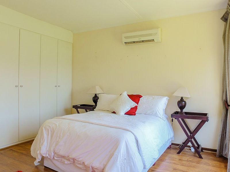 A well-lit bedroom featuring laminate flooring, built-in cupboards for storage, and a wall-mounted split-system air conditioning unit.