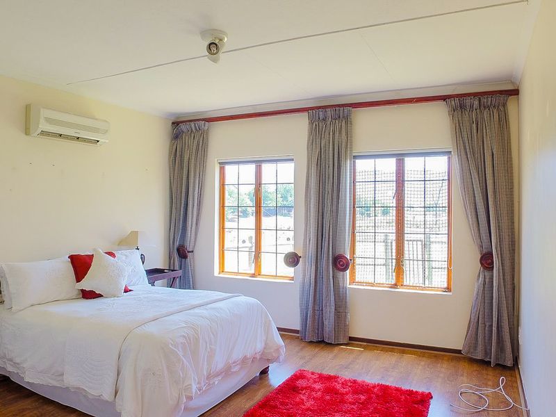 A well-lit bedroom featuring laminate flooring, wooden window frames, and a wall-mounted air conditioning unit.